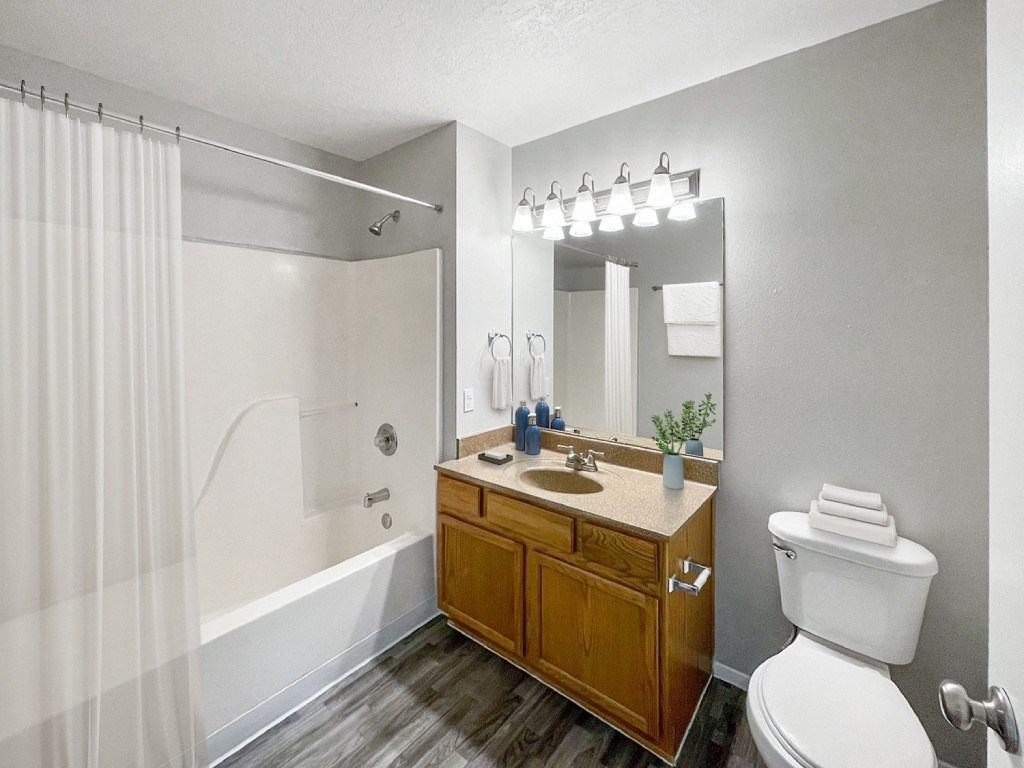A bathroom with a white toilet, a wooden vanity, and a shower with a white curtain.